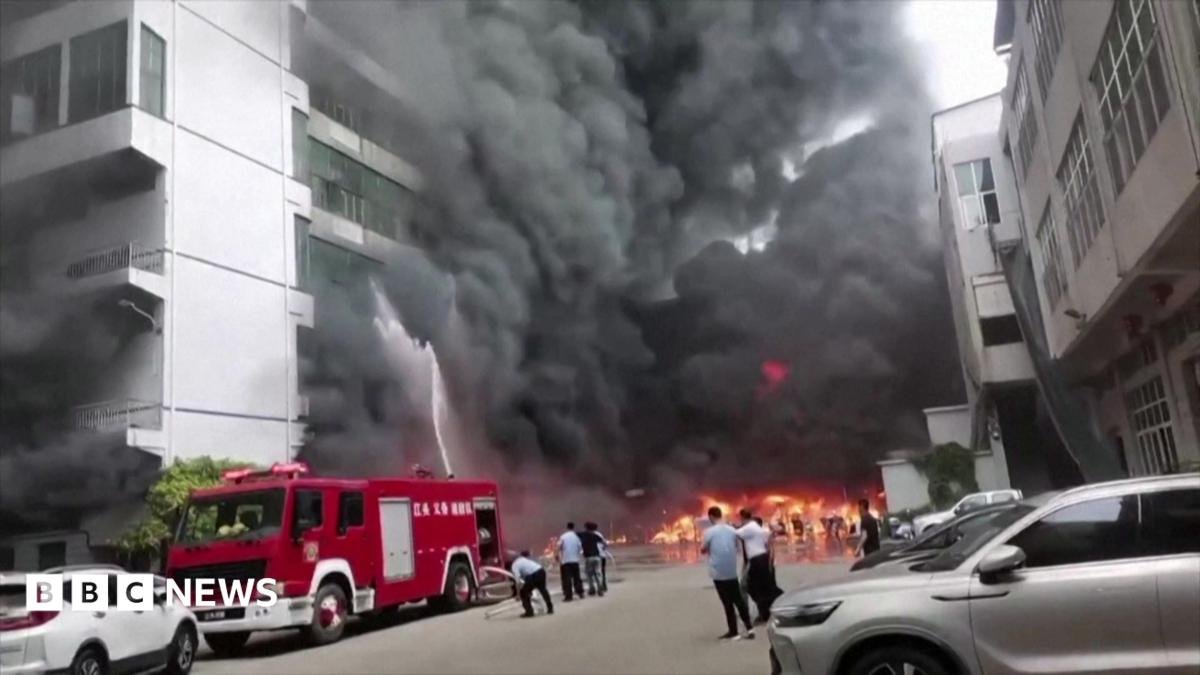 Plumes of black smoke and flames can be seen as a fire truck sprays a burning building with water