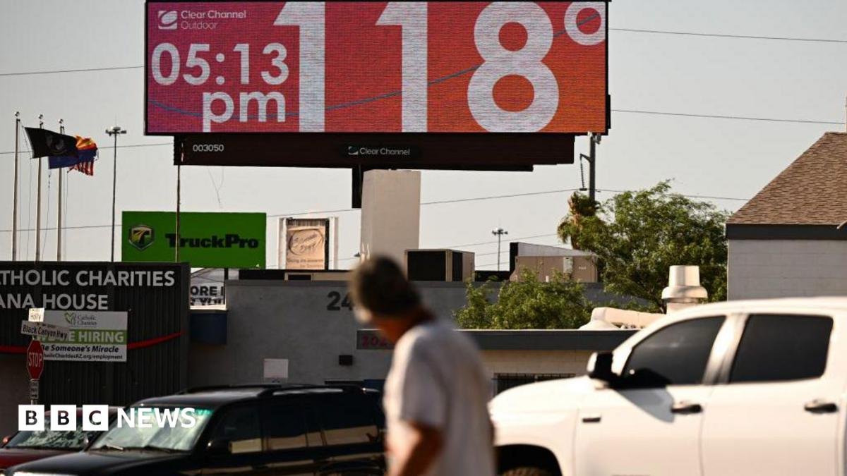 Man walks through road and looks up at sign that says 118 degrees and 05:15 pm