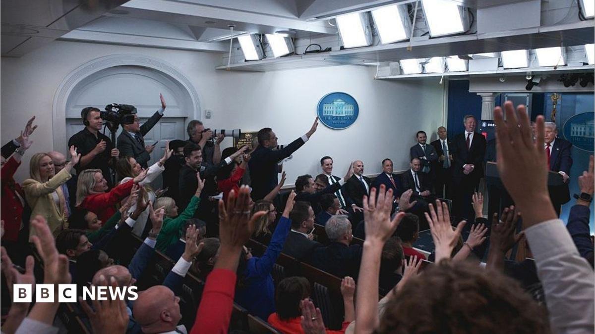The White House press room full of reporters with their hands raised