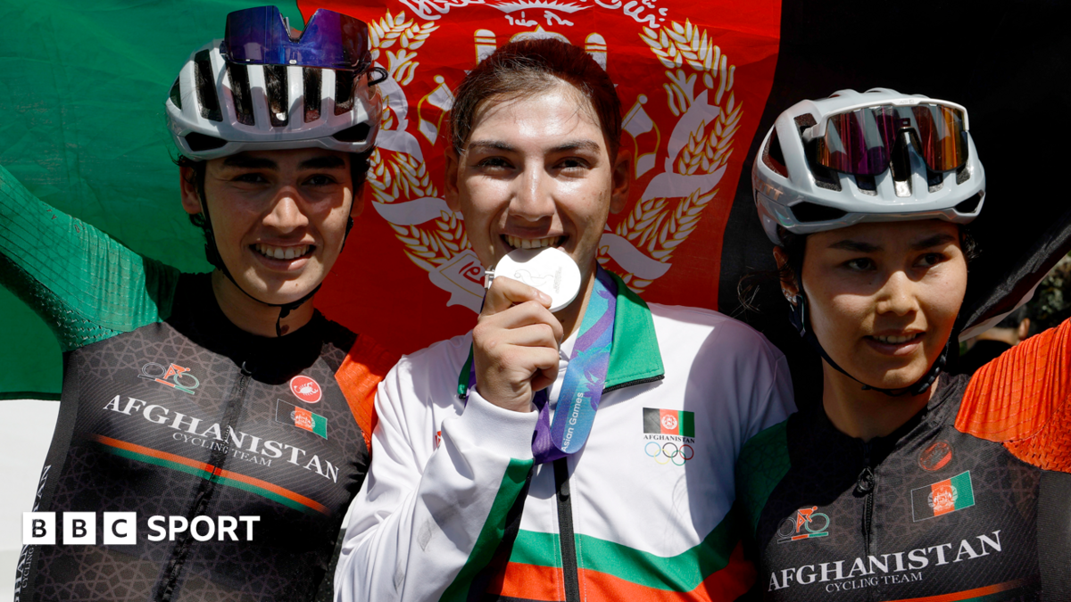 Fariba Hashimi pretends to bite her medal after winning the Aichi-Nagoya Asian Games women's cycling road race silver in Shinshiro, as she stands between two Afghanistan fellow riders