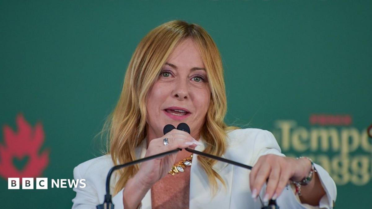 Italian Prime Minister Giorgia Meloni, who has long blonde hair and is wearing a white jacket, speaks into a microphone at an event on 20 September.