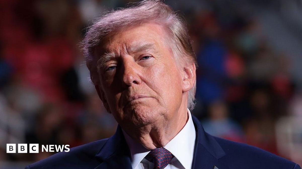 Donald Trump stands in front of a blurred crowd.